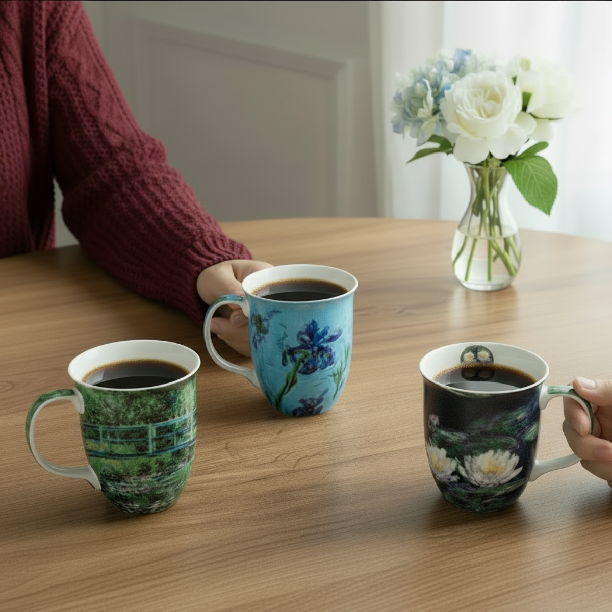 3 fine bone china mugs with monet-inspired designs are displayed on a dining table with two people sitting around the table