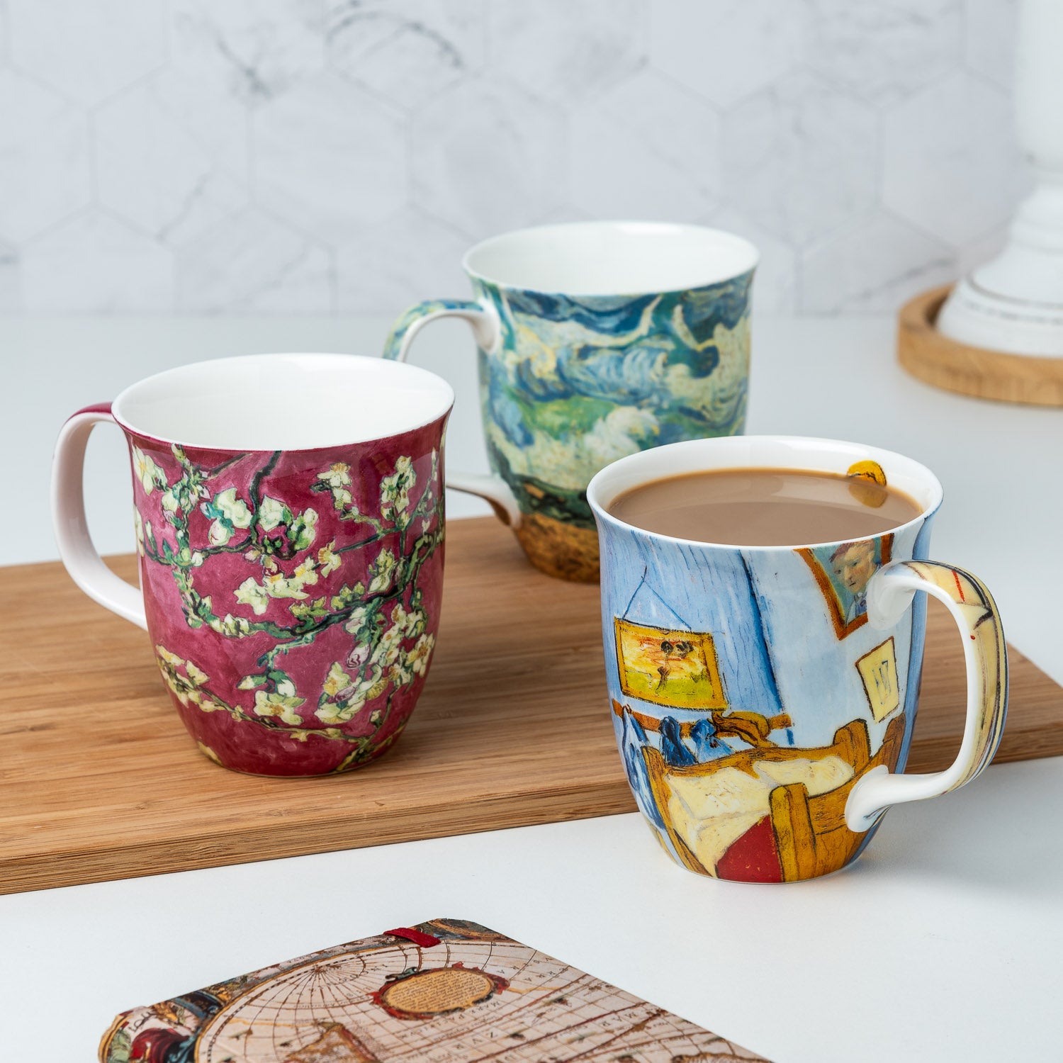 Van Gogh Encore Java mug bundle of three featuring Wheatfield with Cypresses Bedroom at Arles and Almond Blossom Red painting, lifestyle image styled on a countertop with coffee 