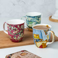 Van Gogh Encore Java mug bundle of three featuring Wheatfield with Cypresses Bedroom at Arles and Almond Blossom Red painting, lifestyle image styled on a countertop with coffee 