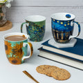 Van Gogh set of three featuring Starry Night over the Rhône Sunflowers and Irises designs Java Mug, lifestyle image styled on a countertop with cappuccino and cookies