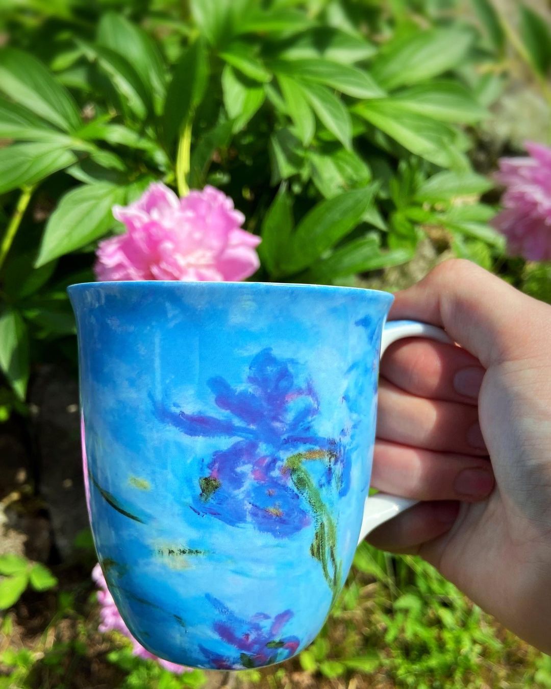 Claude Monet Lilac Irises Java Mug, lifestyle image shown in a garden